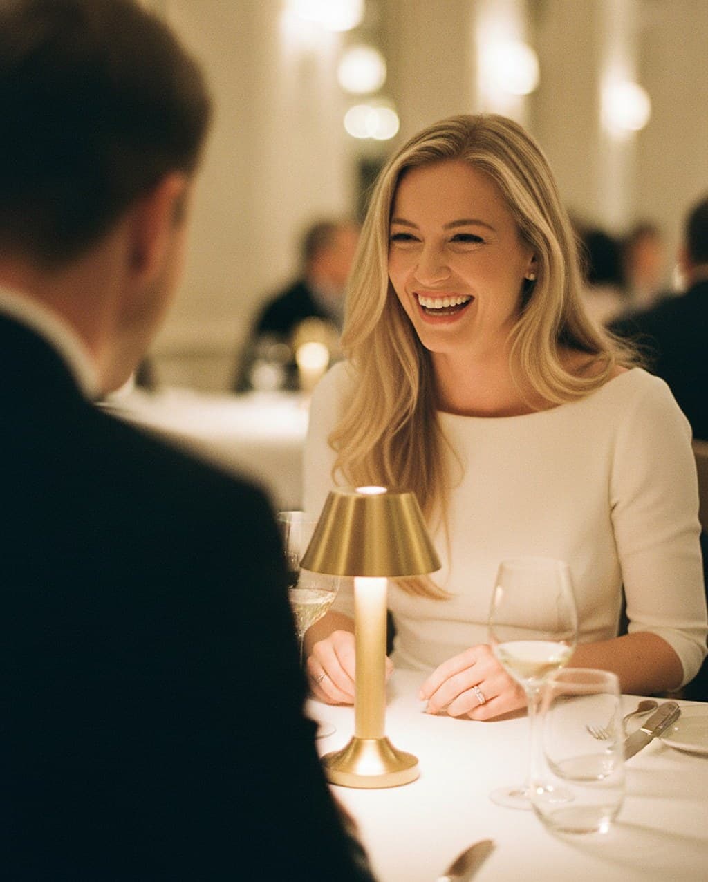 A woman in a white dress laughing across a candlelit restaurant table, her date seen only from behind — models, not patients