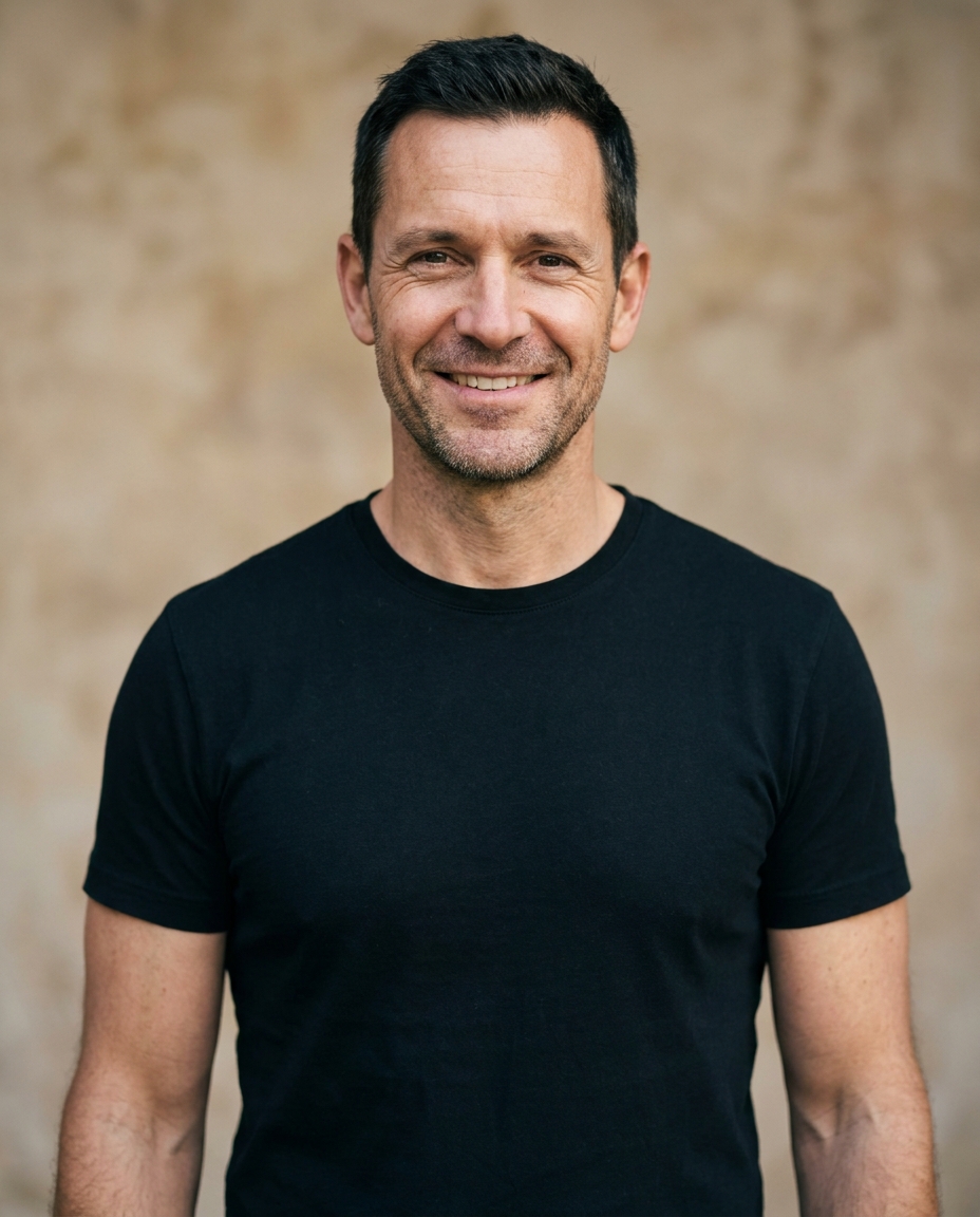 Man in his mid-forties, broader shoulders, black crewneck, slight natural smile, steady eye contact